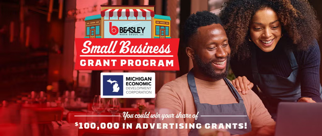 A man and woman in navy overalls smile down at a laptop. Text reads "You could win your share of 100k in advertising grants!"